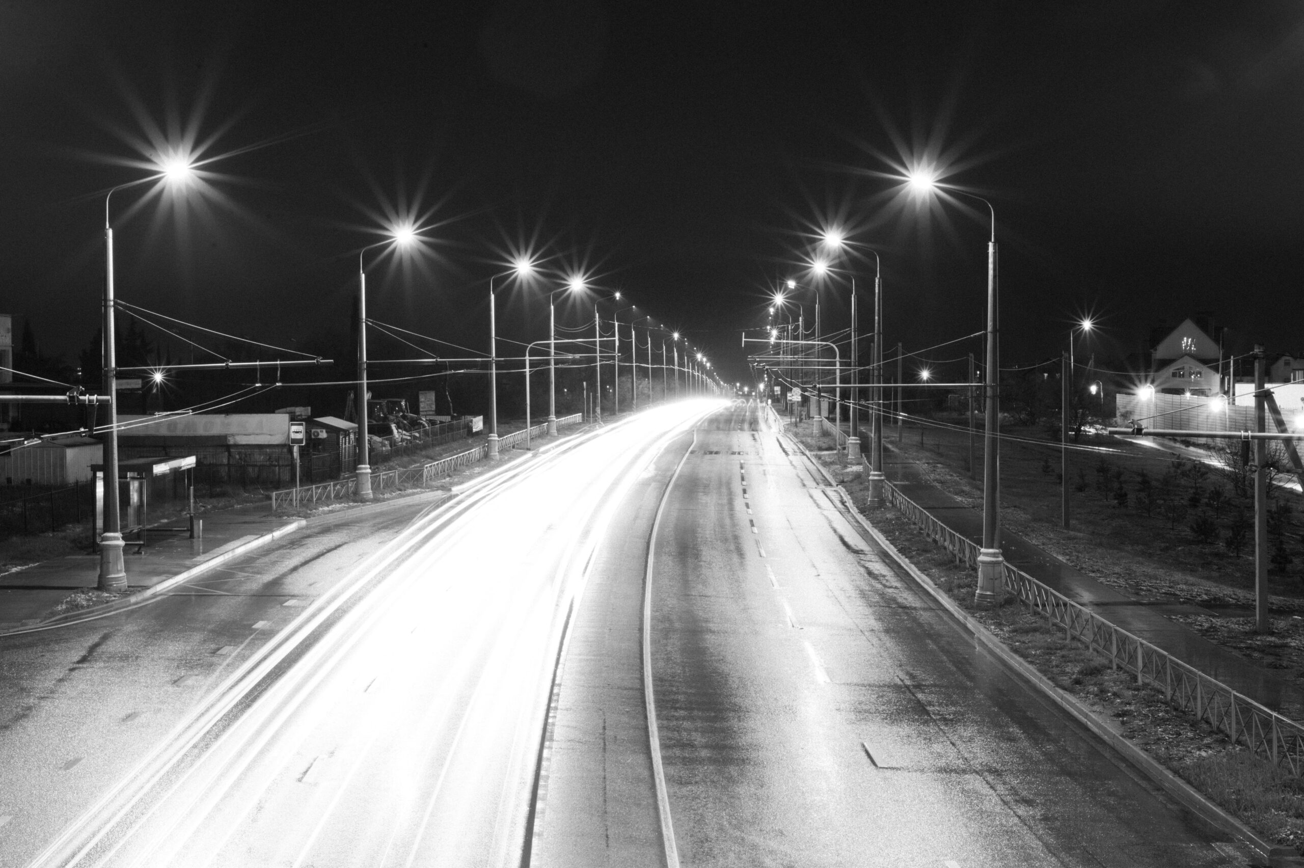 Dynamic long-exposure shot of an empty highway with light trails under street lamps at night.